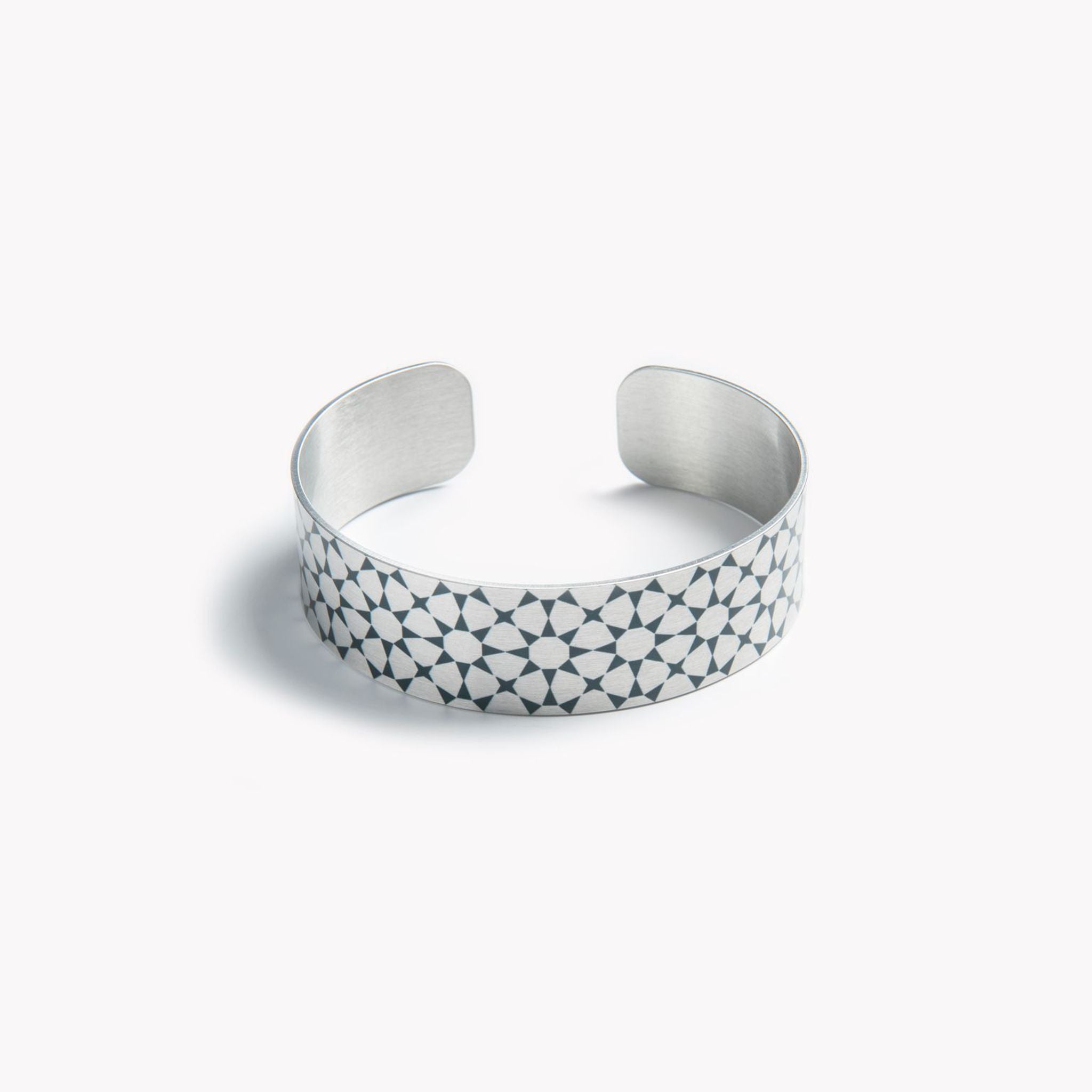 An intricately detailed aluminium cuff bracelet with a black star pattern.