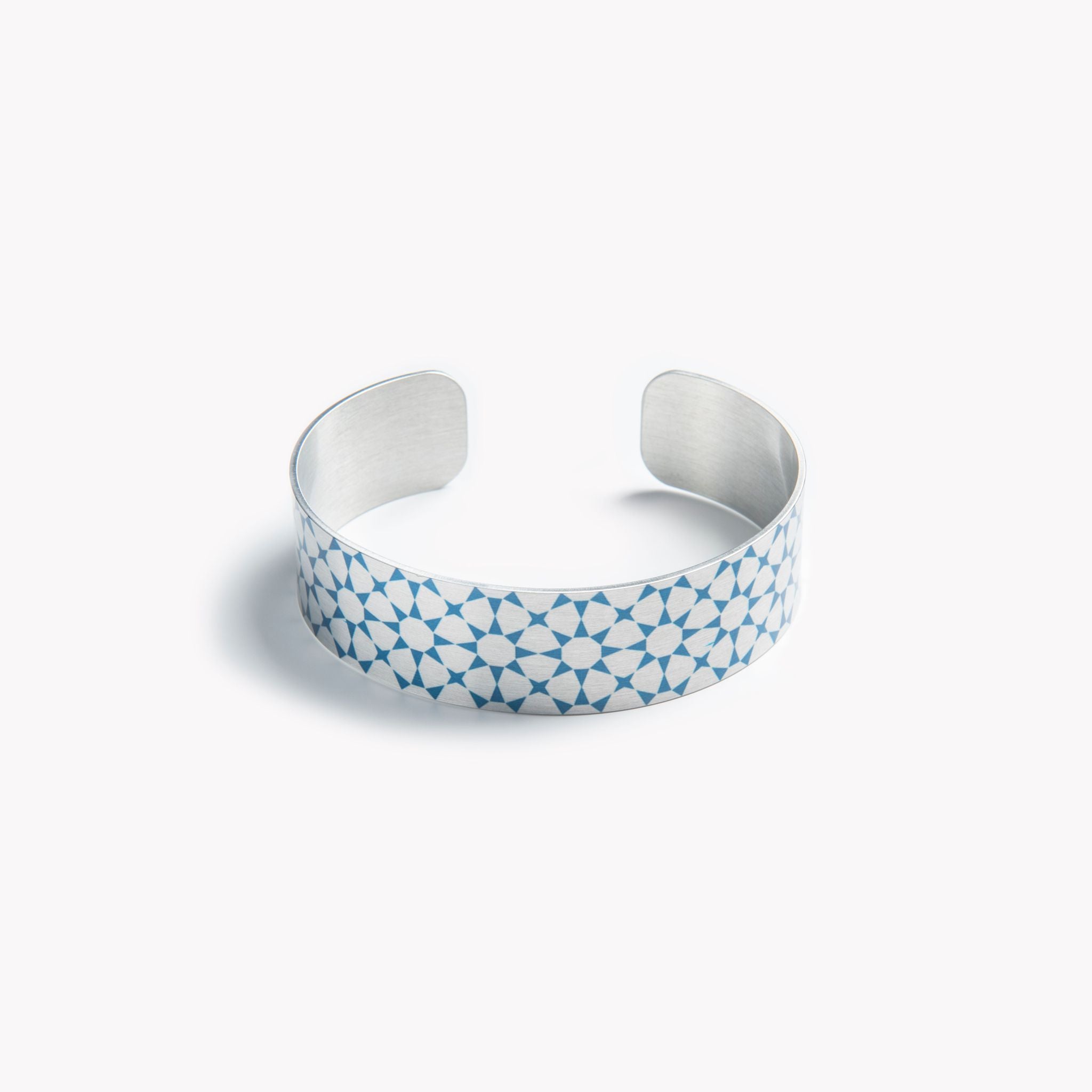 An intricately detailed aluminium cuff bracelet with a teal star pattern.