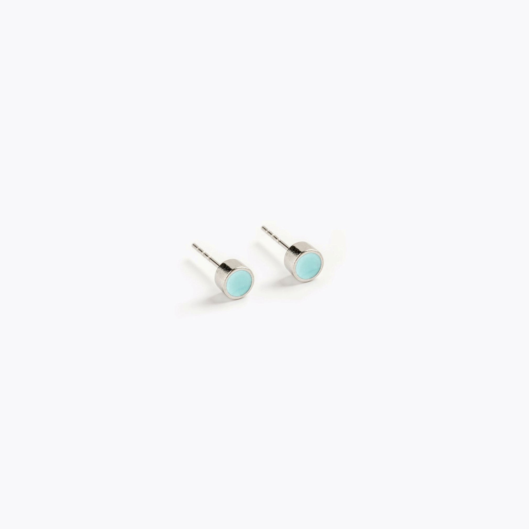 A simple pair of small, turquoise, circular stud earrings.
