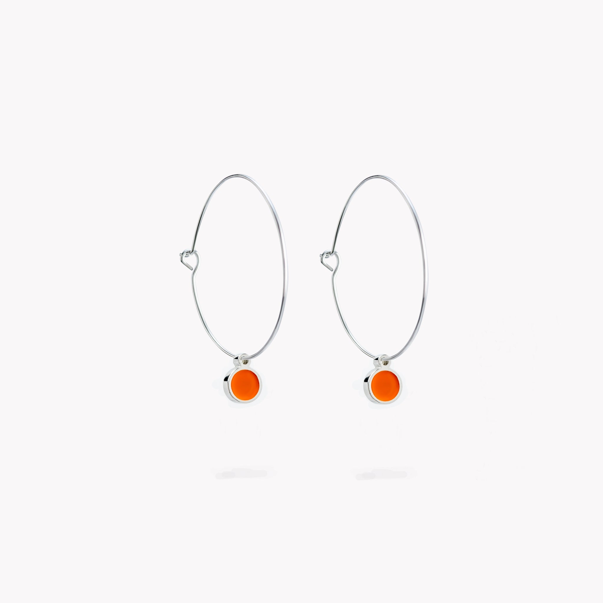 A pair of simple hoop earrings, each with a bright orange hanging circular form.