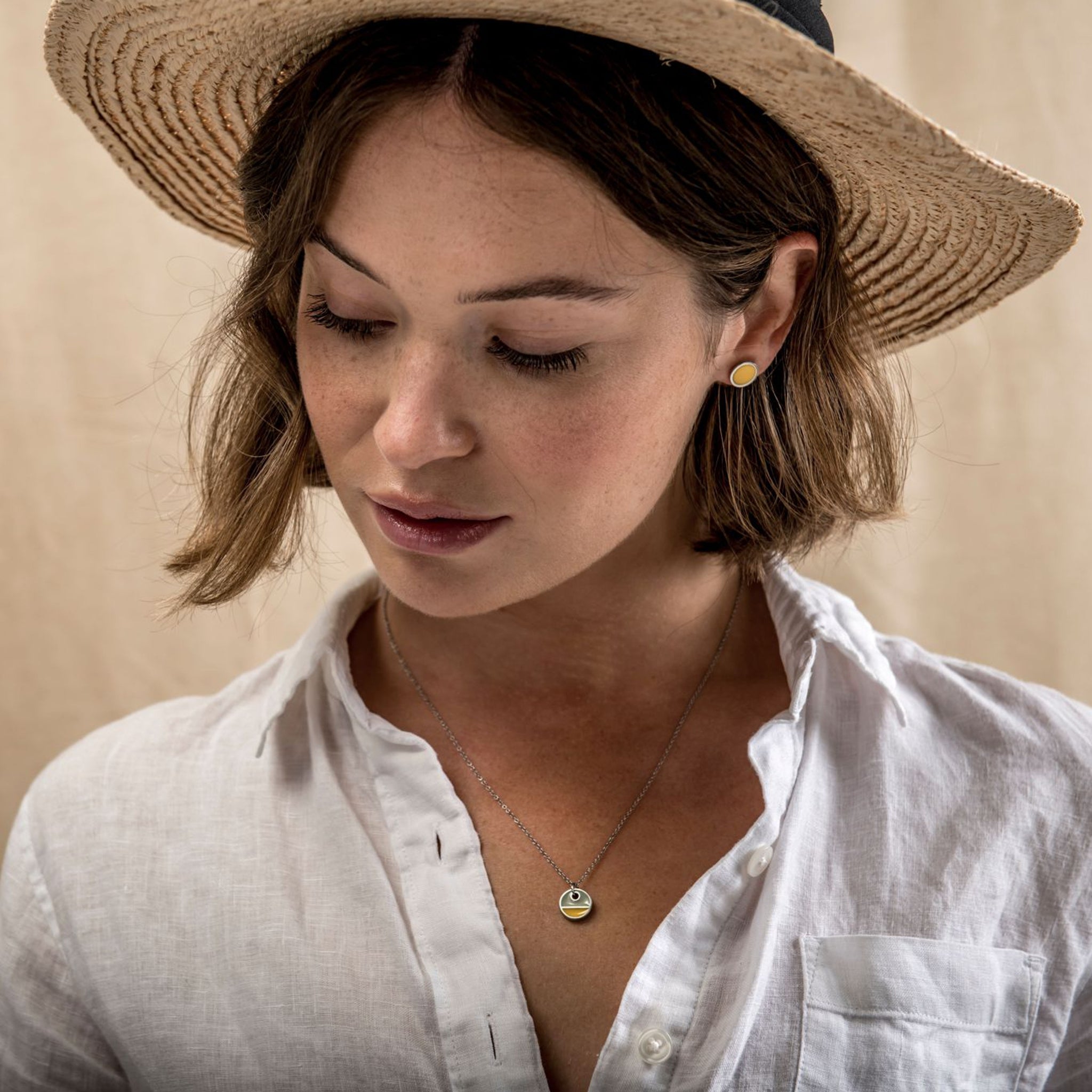 Fashion model wearing a simple, yellow, circular stud earring.