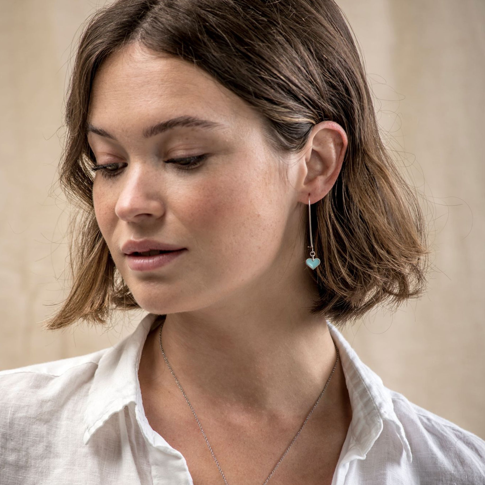 Fashion model wearing a simple, turquoise, heart shaped drop earrings.