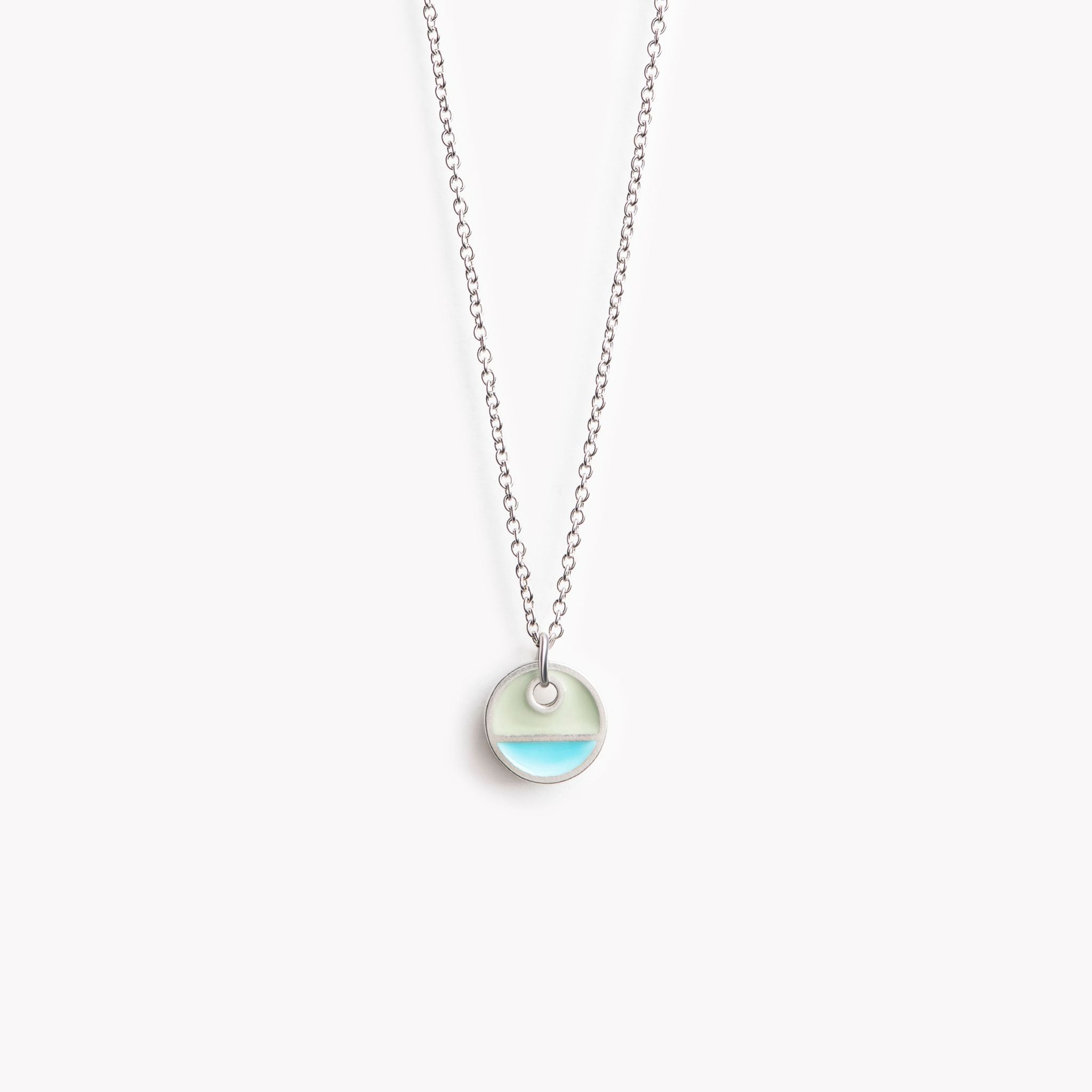 A simple circular pendant necklace with a horizontal division. In turquoise and grey.